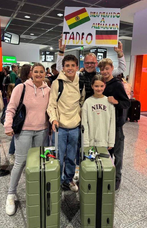 Drei Austauschschüler mit Koffern werden am deutschen Flughafen mit Schildern begrüßt